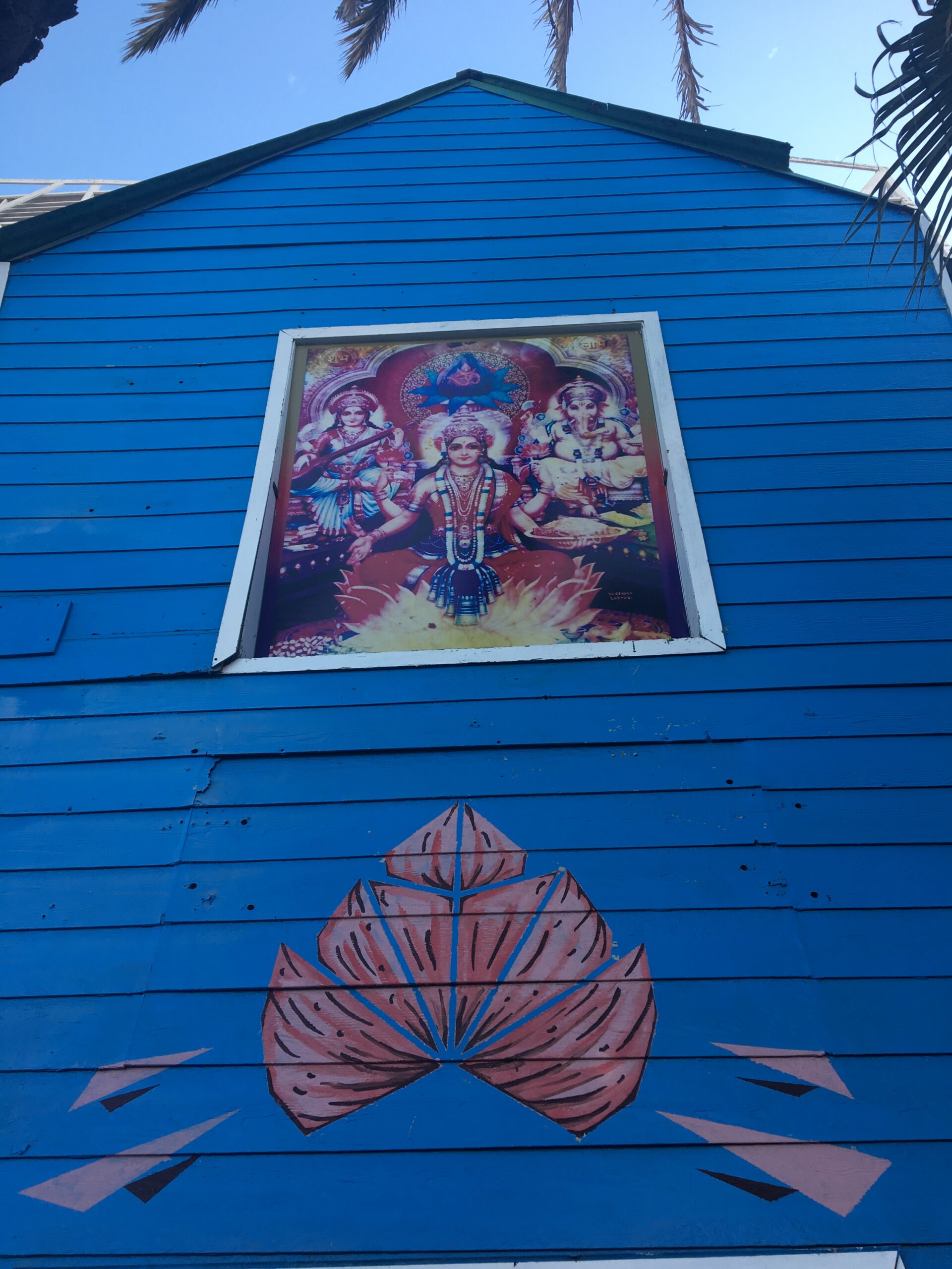 Hindu deities Lakshmi, Saraswati, and Ganesh displayed on a bright blue building facade in Rosarito, Baja California, Mexico